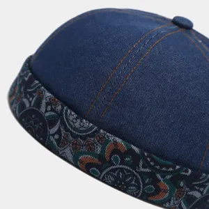 Close-up of blue washed denim brimless hat, detailed patterned contrast brim and orange stitching.