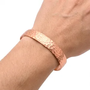 Close-up detail of the elegant hammered copper cuff bracelet showing fine texture worn on wrist.