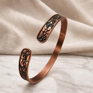 Detailed shot of an open-end copper bracelet featuring vintage floral and scroll engravings.