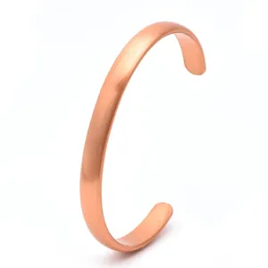Close-up detail of minimalist brushed copper cuff bracelet surface texture and open design.