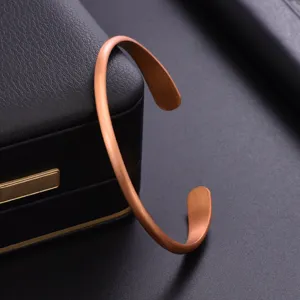 Close-up detail of a minimalist matte brushed copper cuff bracelet on dark display surface.