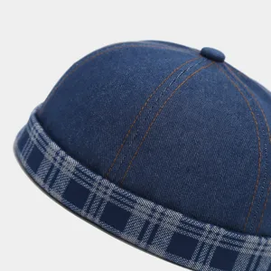 Close-up view of a blue denim docker cap, featuring contrast orange stitching and a stylish plaid brim.