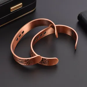 Closeup detail of vintage red copper magnetic bracelet with tree of life pattern and open design.