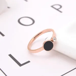 Close-up of minimalist rose gold titanium steel ring with black disc and sparkling crystal.