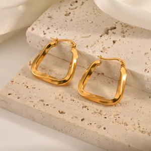 Detailed close-up of geometric gold-plated twisted hoop earrings on textured stone background.