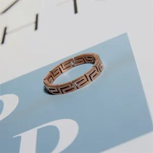 Details of a stylish rose gold titanium steel ring with hollow Greek key geometric pattern.