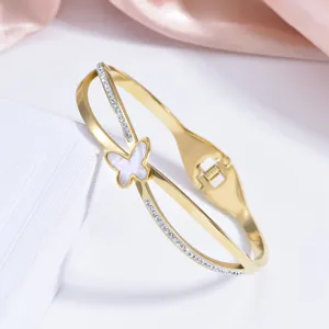Détail de bracelet jonc croisé en acier doré avec papillon en coquille et strass.