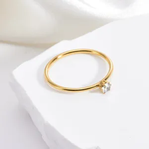 Close up detail of minimalist gold stainless steel ring with single clear zircon stone.