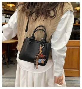 Chic black leather bucket bag for women with cute bear pendant, versatile crossbody bag.