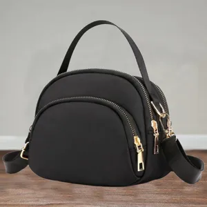 Detail view of black nylon mini shell crossbody bag, featuring gold tone zippers and strap.