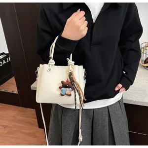 Chic white leather bucket bag with cute bear charm and woven strap, perfect for daily wear.