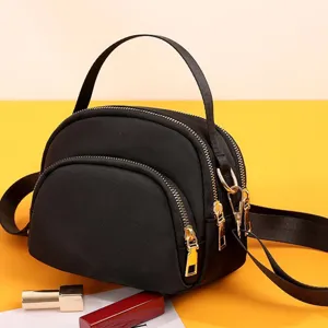 Detail shot of black nylon mini shell crossbody bag showing golden zippers and hardware clearly.