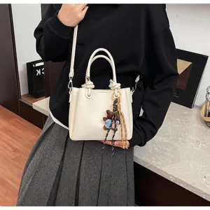 White soft leather bucket bag detail featuring a cute bear pendant and braided charm strap.