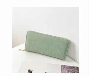 Vista detallada de una cartera larga de piel sintética verde con acabado mate y cremallera.