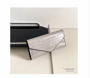 Detailaufnahme einer eleganten grauen Kroko-Muster Lackleder-Langbörse mit Kuvertklappe.