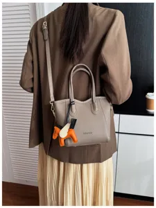 Vista dettagliata dell'elegante borsa a secchiello tortora con manici e ciondolo.