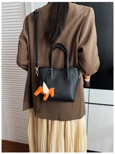 Primo piano della borsa in pelle nera con manici e ciondolo cavallo alato arancione.