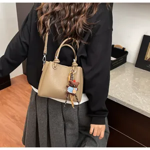 Khaki leather bucket bag with cute bear pendant, stylish shoulder bag for women daily commute.