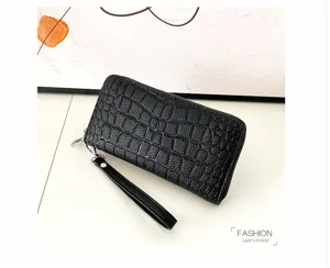 Vue détaillée d'un portefeuille zippé long en motif crocodile noir avec dragonne sur surface.