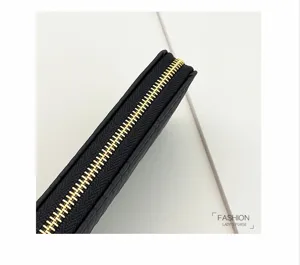 Close-up detail of black long wallet with golden zipper and textured embossed leather surface.