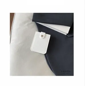 Λεπτομερής εικόνα λευκής θήκης καρτών από τσόχα με κουμπί σε μινιμαλιστικό φόντο υφάσματος.