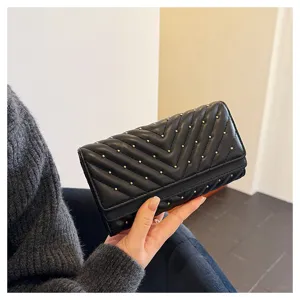 Vista dettagliata di un portafoglio nero trapuntato con cuciture chevron e borchie metalliche.