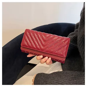 Primo piano dettagliato del portafoglio lungo bordeaux trapuntato con borchie metalliche.