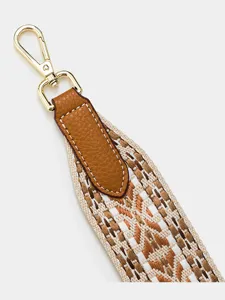 Close-up detail of wide woven bag strap with brown leather connector and gold swivel hook.