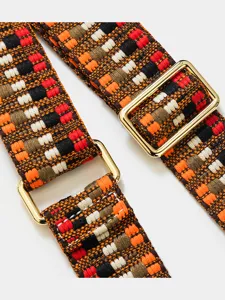 Gros-plan d'une bandoulière tissée géométrique colorée avec quincaillerie dorée brillante.