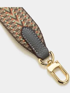 Woven bag strap with geometric V-pattern, leather ends, and gold metal clasp for crossbody bags.