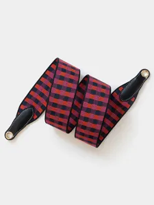 Close-up of colorful plaid webbing strap, featuring durable black leather ends and metal eyelets.