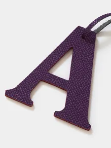 Closeup purple cowhide leather letter A bag charm detail showing fine texture and edges.