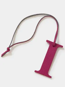 Detalle colgante letra I de cuero, accesorio de bolso textura fucsia llavero.