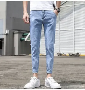 Detail view of men's light blue slim cropped denim jeans paired with white casual shoes outdoors.