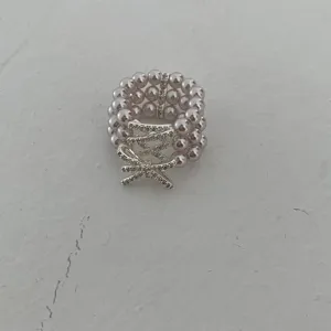 Close-up detail of the three-layer pearl ring showing the sparkling crystal bow and elastic band design.