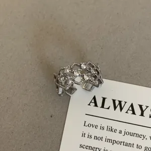 Zilverkleurige open ring met sprankelende zirkonia, ingewikkeld hol design, elegant sieradendetail.
