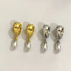 Detailopname van vintage gezicht reliëf oorbellen met parelhangers in goud en zilverkleur.