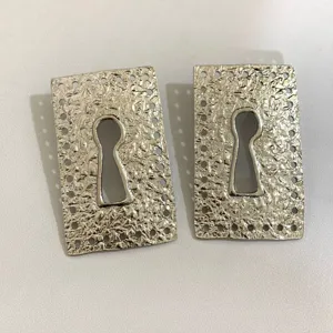 Detailed view of retro silver metallic keyhole earrings with textured finish and perforated border.