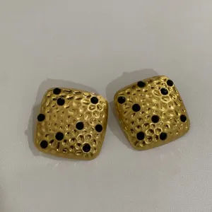 Gedetailleerde close-up van vintage getextureerde gouden oorbellen met zwarte steenaccenten.