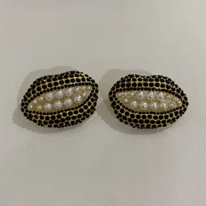 Detailopname van liptype oorbellen bezet met zwarte strass-steentjes en witte parels.