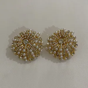 Gedetailleerde close-up van vintage goudkleurige oorbellen met kunstparels en strass-steentjes.