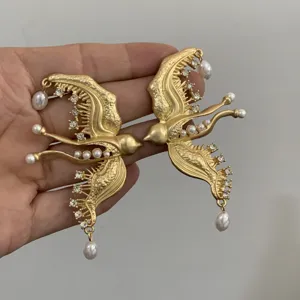 Overdreven gouden vogel statement oorbellen met sprankelende strass stenen en elegante parels.