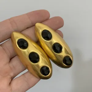 Detailopname van grote gouden geometrische oorbellen met drie zwarte geslepen stenen.