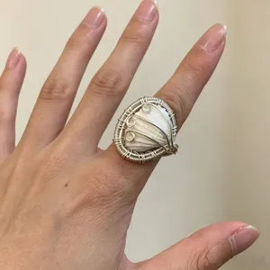 Nahaufnahme des handgemachten drahtverwickelten Muschelrings mit offenem Metallband Design