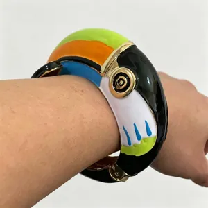 Close-up detail van een kleurrijke geëmailleerde toekan gevormde metalen armband om pols.
