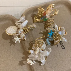 Nahaufnahme handgefertigter drahtgewickelter Muschel- und Seestern-Ringe im Strand-Design.
