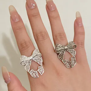 Close-up detail van de zilveren holle strikring gedragen aan de vinger, unieke artistieke stijl.