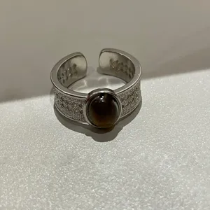 Zilverkleurige open ring met opengewerkt filigraan patroon en ovale donkere imitatiesteen.