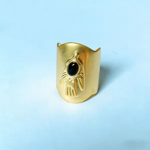 Detailopname van brede gouden statement ring met gegraveerd handontwerp en zwarte steen.