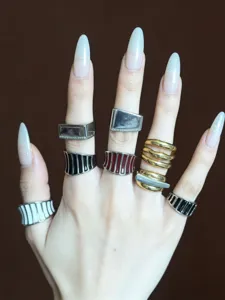 Primo piano di vari anelli a righe smaltate e anelli in metallo geometrici sulla mano.